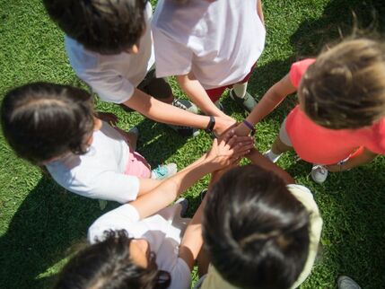 A group of children standing in a circle with their hands on top of each others.