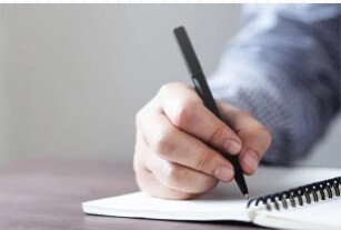 A white hand holding a pen to a notebook