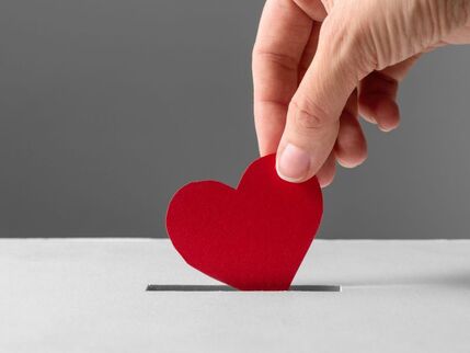 Donation box with a red heart being pushed in by a hand