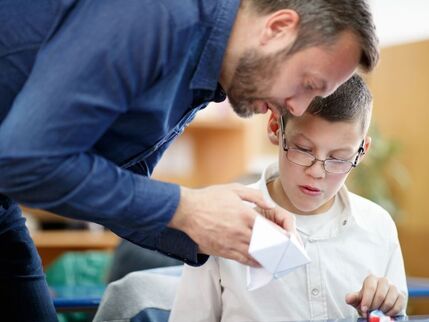 A man leaning over a child to help with learning