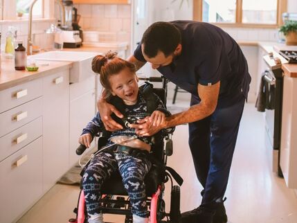 A Father leaning over his smiling daughter in a wheelchair 