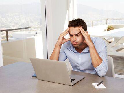 Man with hands on head looking at computer 