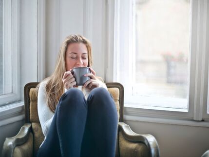 Woman sitting in a chair sipping from a mug with her eyes closed 