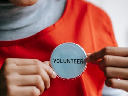 A woman's torso with a red bib holding out a badge that says volunteer 