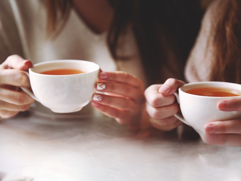 Two set of ladies hands holding two cups of tea close to each other